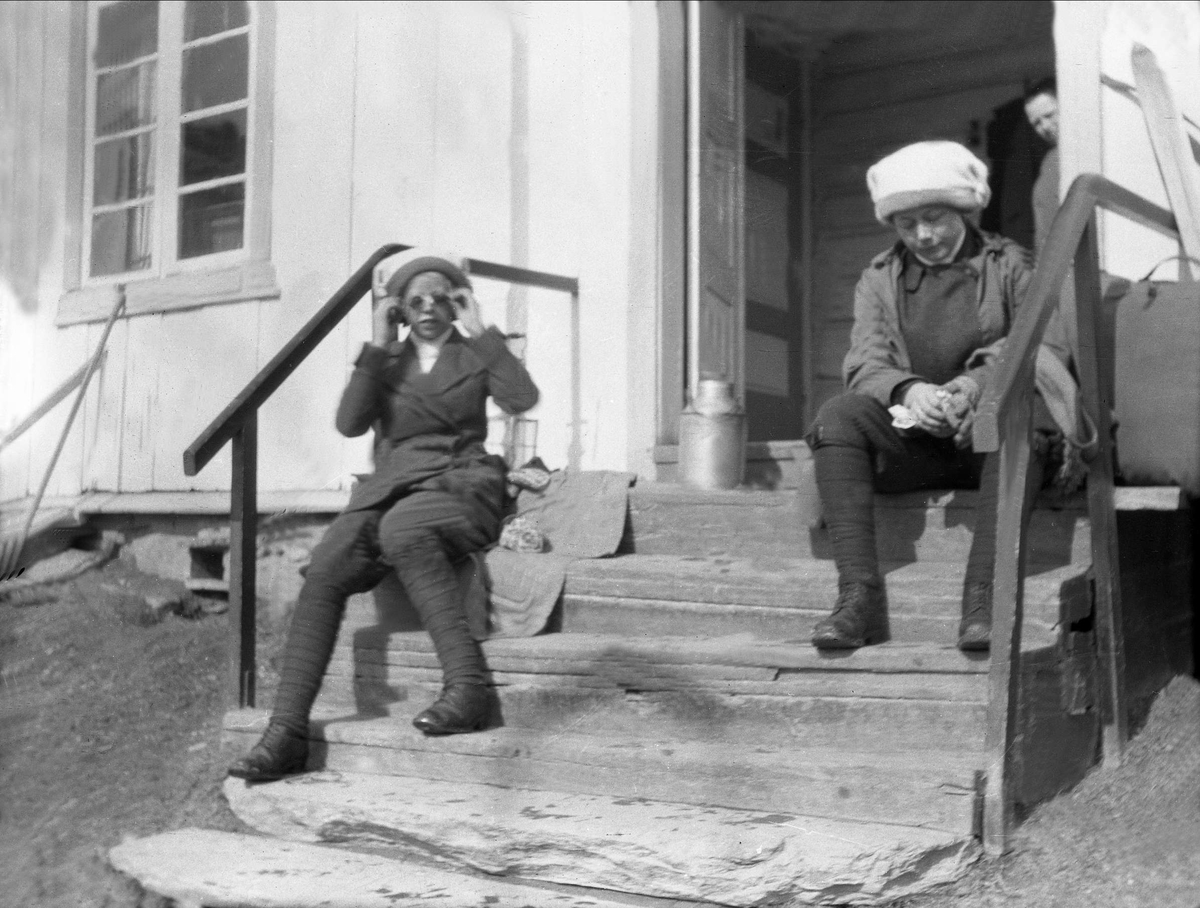 To kvinner sitter på en trapp utenfor et hus. Robsahm og Lund.