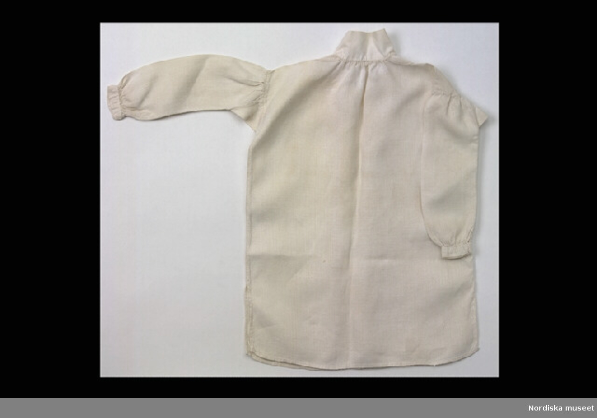 Inventering Sesam 1996-1999:
a)  L  26  cm
b)  L  31  cm
2 st skjortor av linne. lång ärm och krage. 
Tillhör docka inv 108.264. 
Birgitta Martinius 1996