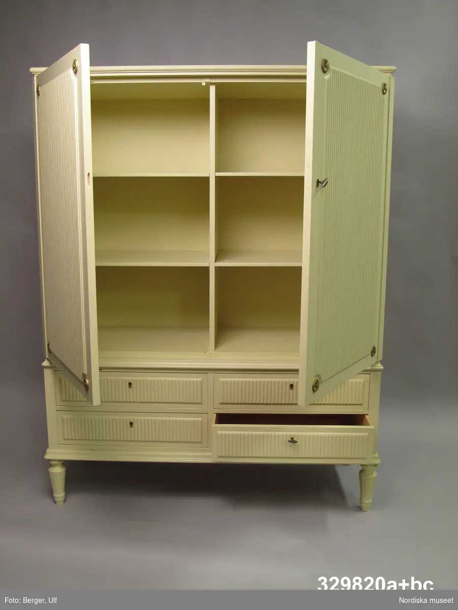 Skåp (a+), gustaviansk stil, Ikea 1961-62, benvit lack, sprutlackerat, med förgyllda detaljer, rektangulärt stående form. Två nycklar av gulmetall (b-c). Del av matsalsmöblemanget "Desirée", se även stolar, 6 st (inv.nr 329.818+), och matbord (inv.nr 329.819a-f).

Av furu med rygg av björkplywood. Svarvade, nedåt avsmalnande kannelerade ben av björk. Överst två dörrar samt därunder två lådvarv med vardera två lådor. På dörrarna fält med räfflad dekor, i hörnen skurna fleuroner, målade i guldfärg, pålimmade. Fyra lösa hyllplan av furu. Vitlackerat invändigt. Dörrarna på pianogångjärn av mässing. Lådor, maskinsinkade. Lådförstycken och sidor av furu, botten av björkplywood. På lådförstyckena räfflad dekor, sannolikt pålimmad .
Nyckelbussningar på dörrarna av mässing. 2 st nycklar, längd 4 cm. 
Anm: En nyckelbussning saknas.
/Anna Womack 2010-01-20
