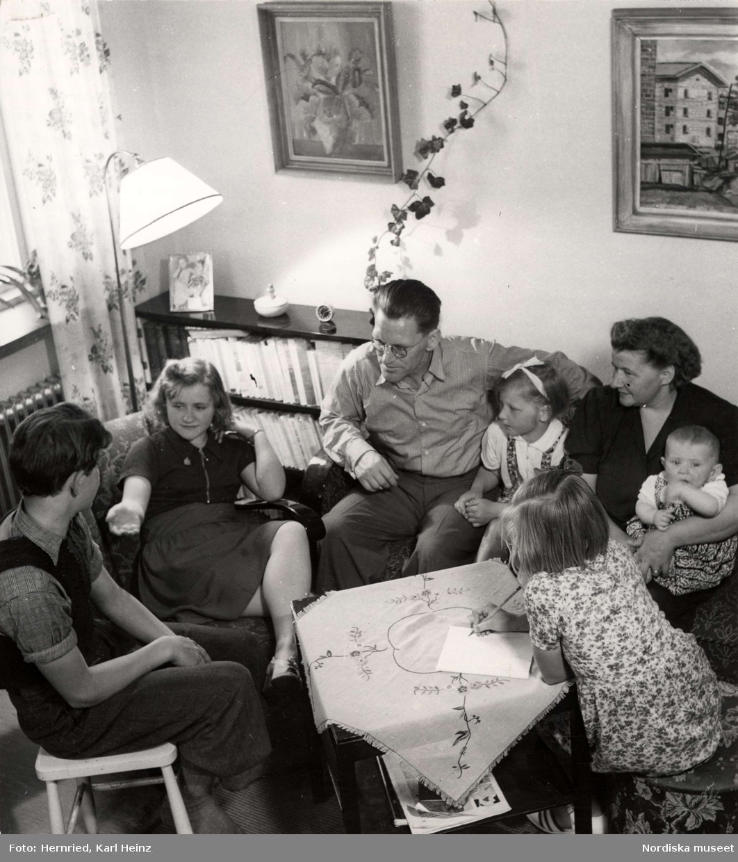 Familj sitter runt ett bord i vardagsrum och samtalar.