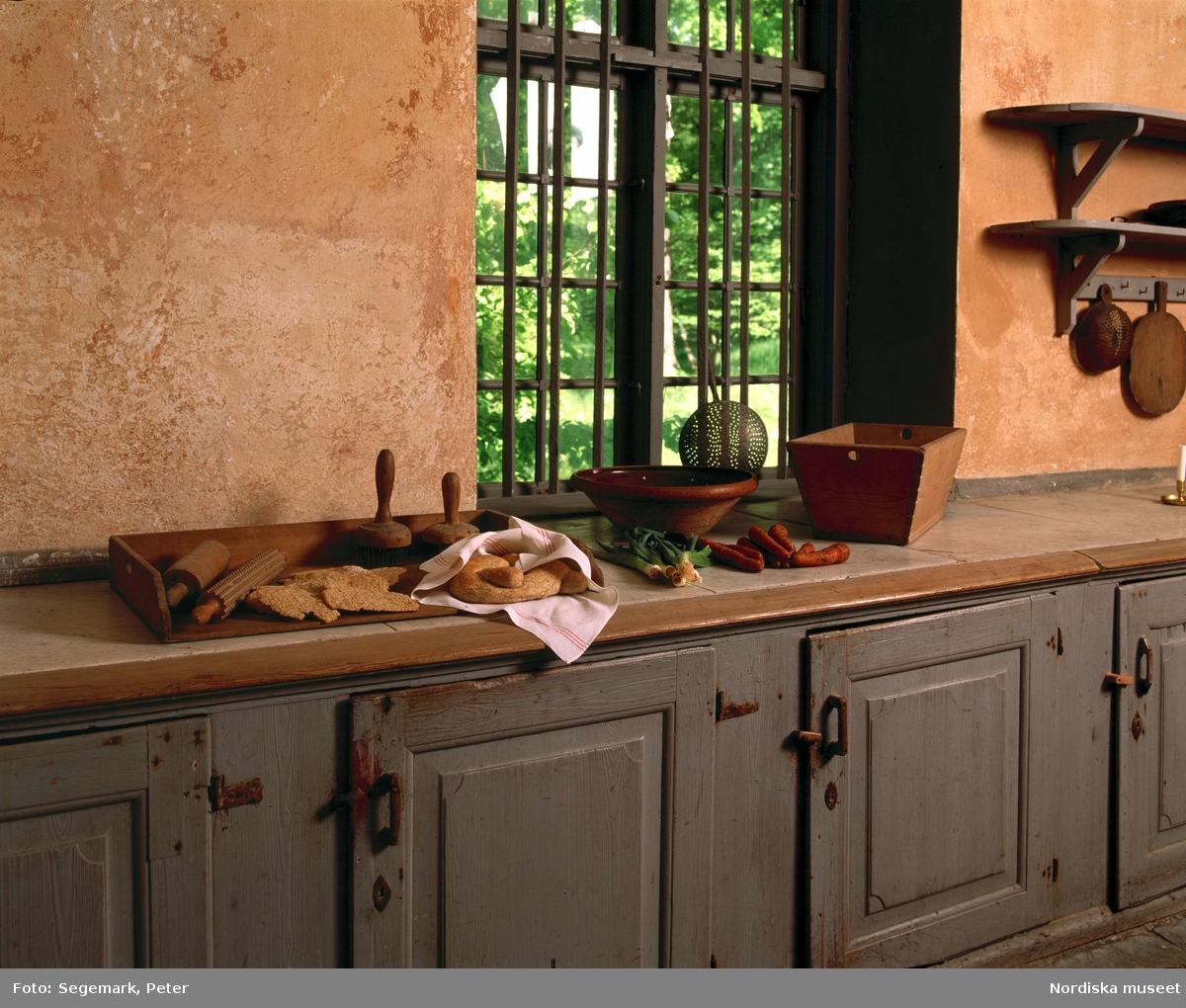 Svindersvik. Bänk med marmorskiva i köket där bröd och grönsaker samt skålar och redskap för matlagning ställts fram.