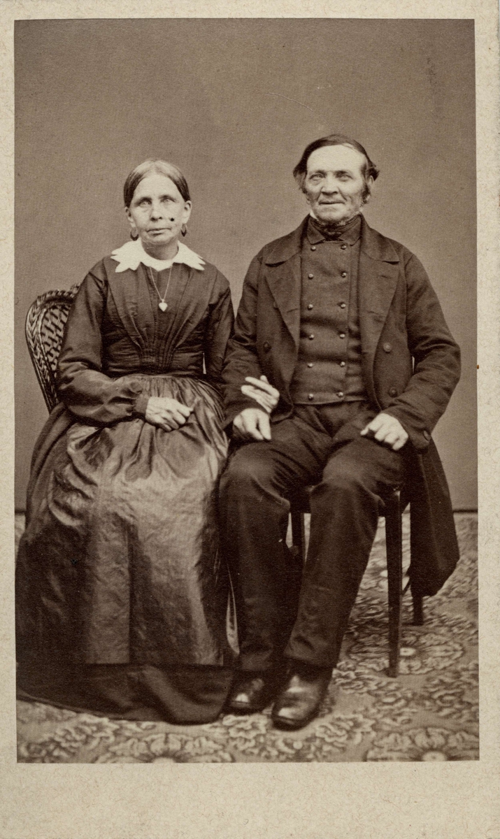 Ett par poserar sittande på stolar. Kvinnan håller mannens arm. Från Höj, Harjagers härad i Skåne. Inv.nr. 18518Q.
