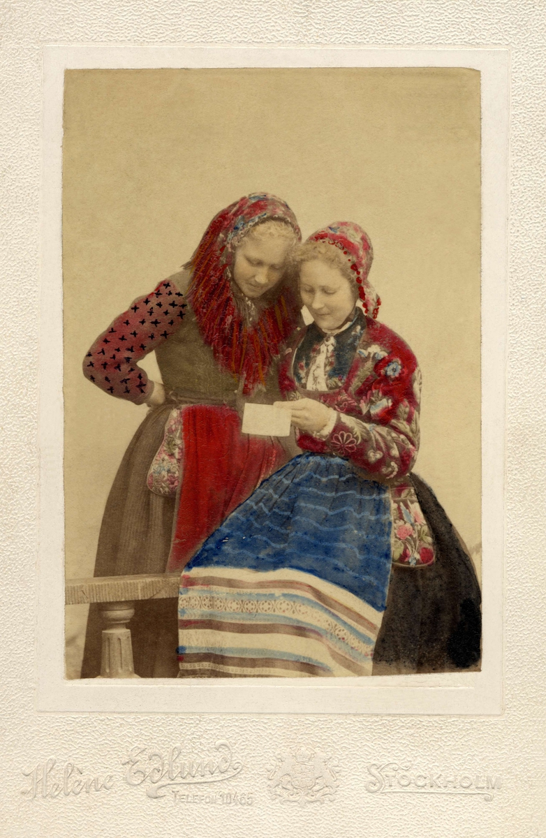 Två kvinnor i folkdräkt, läser ett brev.
