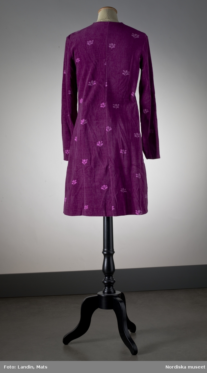 Kort-kort klänning av trikåsammet (plysch) av bomull. Violett med tryckt mönster i ljusare violett kallat "Kvist". 1970-talets början. Mah-Jong AB. Nordiska museet inv nr 313615.