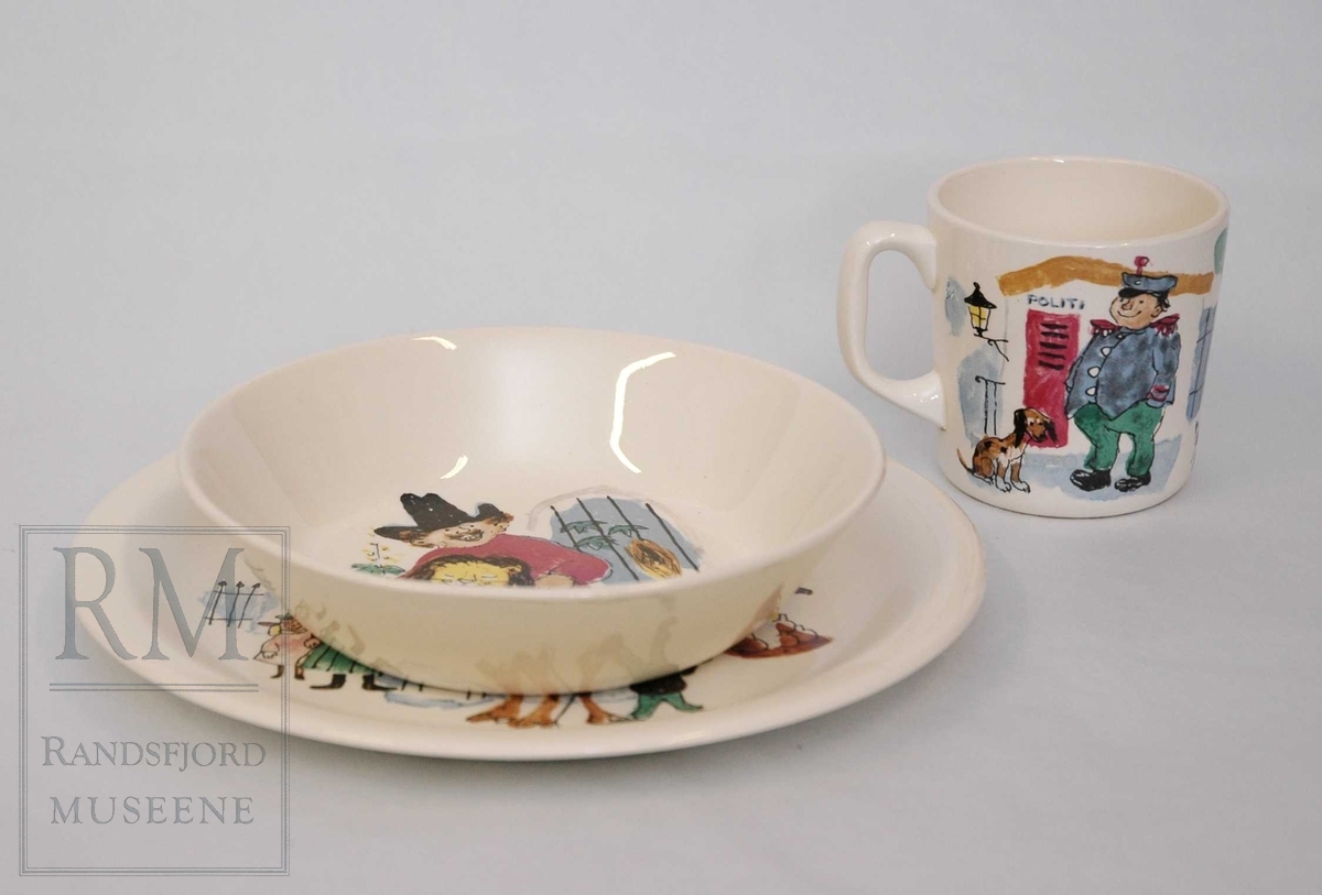 Flat tallerken, dyp tallerken og kopp i hvitt steintøy med fargerik dekor: motiver fra "Kardemommeby" av Torbjørn Egner. Eske med Egners tegninger og teksten til sjørøvervise.