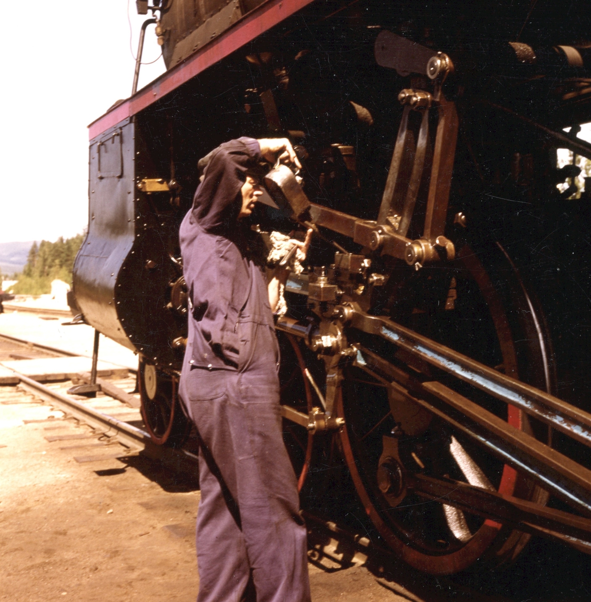 Fyrbøteren smører gangtøyet på domplokomotiv 26c nr. 414 under oppholdet på Koppang stasjon.