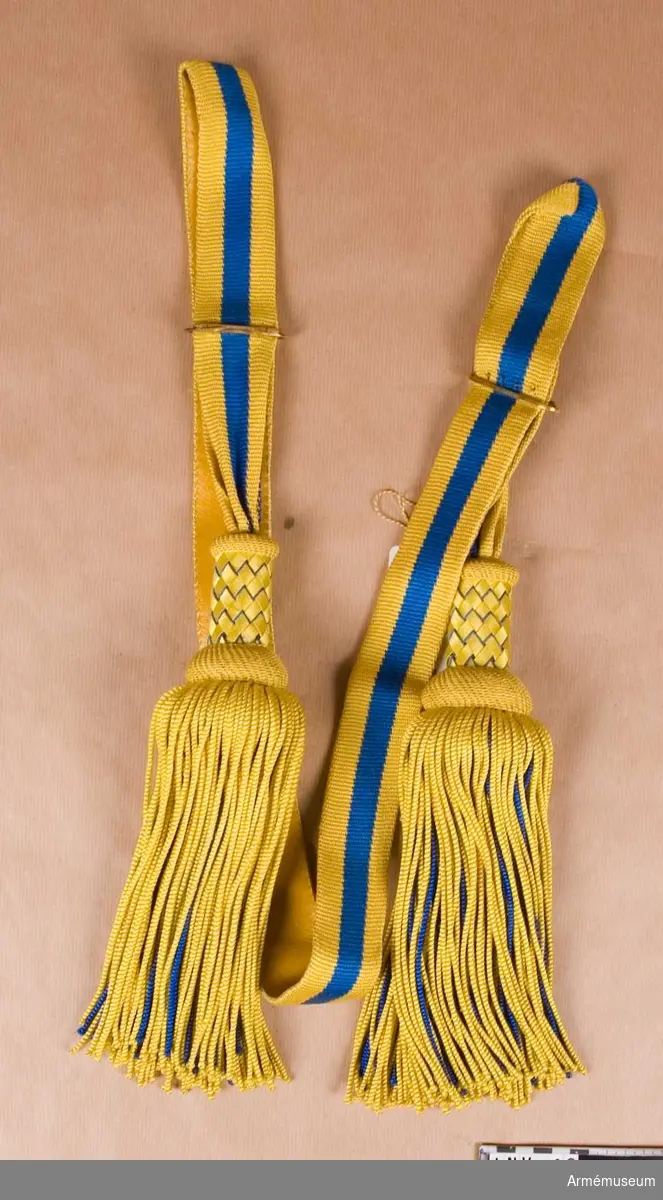 Paradskärp av silke, språngat med 2 gula och en blå rand. 2 tofsar, med flätad överdel i samma färger. Foder av gult skinn.
Har tillhört Gustav VI Adolf (1882-1973).