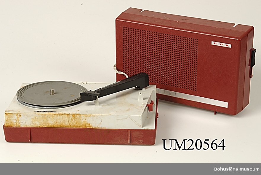 Batteridriven grammofon med högtalare ihopsättbara till bärbar enhet.
Röd och grå plast. De röda plastdelarna har ett lågmält präglat mönster i relief.
Handtaget är grått.

Ett föremål som på 1960-talet hade stor attraktionskraft bland tonåringar.