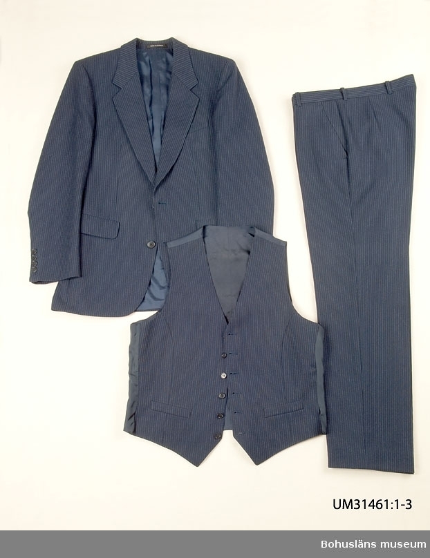 Mörkblå kostymbyxa (UM31461:1) sammanhörande med kostymkavaj (UM31461:1) och kostymväst (UM31461:3).
410 Mått/Vikt  Benlängd 79 cm  Benvidd 21 cm

Kostymbyxa i mörklblå ull med smala kritstreck. Ofodrade. Linning med hällor för bälte, knäpp framtill med slejf. Gylf med dragkedja, Två snedställda sidfickor, en infälld bakficka med dekorknapp. Fickor av vitt bomullstyg. 
På insidan firmaetikett med texten:
"TIGER OF SWEDEN
STORL.
SIZE.
GRÖSSE  B 48.
451 26 UDDEVALLA
På baksidan uppgifter om kvalitet och tvättråd.