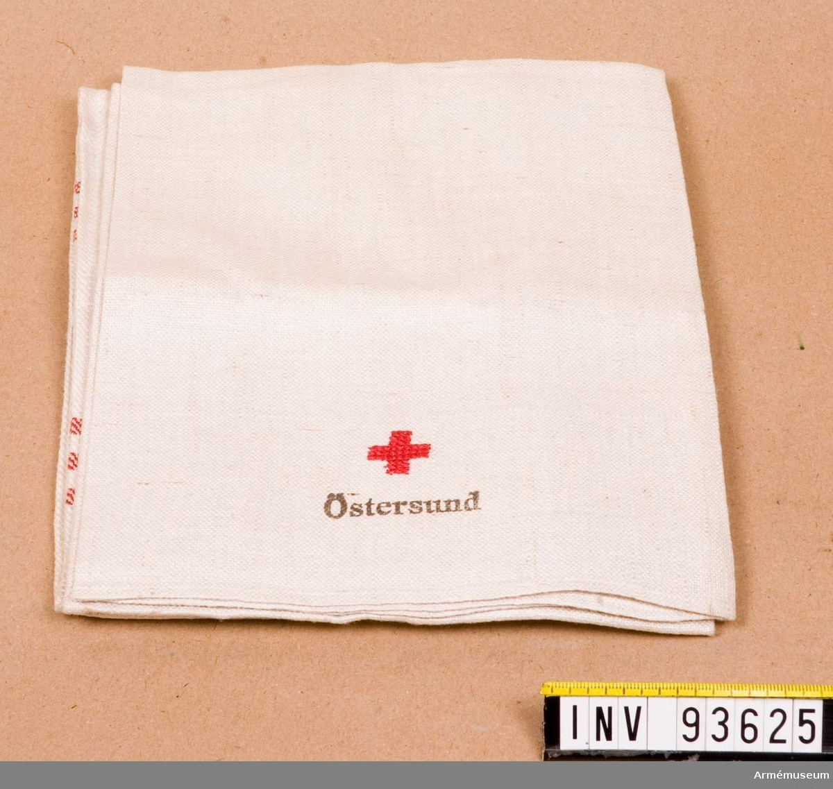 Vit handduk med tre röda ränder märkt med Röda Korset och text.