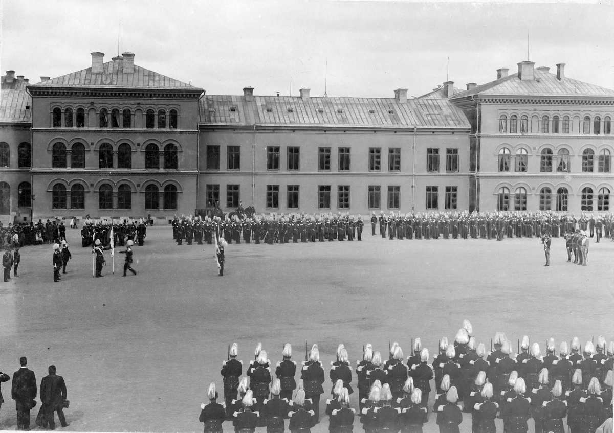 Kung Oscar II delar ut fanor åt Göta livgarde I 2 utanför regementet på Storgatan/Linnégatan i Stockholm. Civila åskådare ser på i bakgrunden.