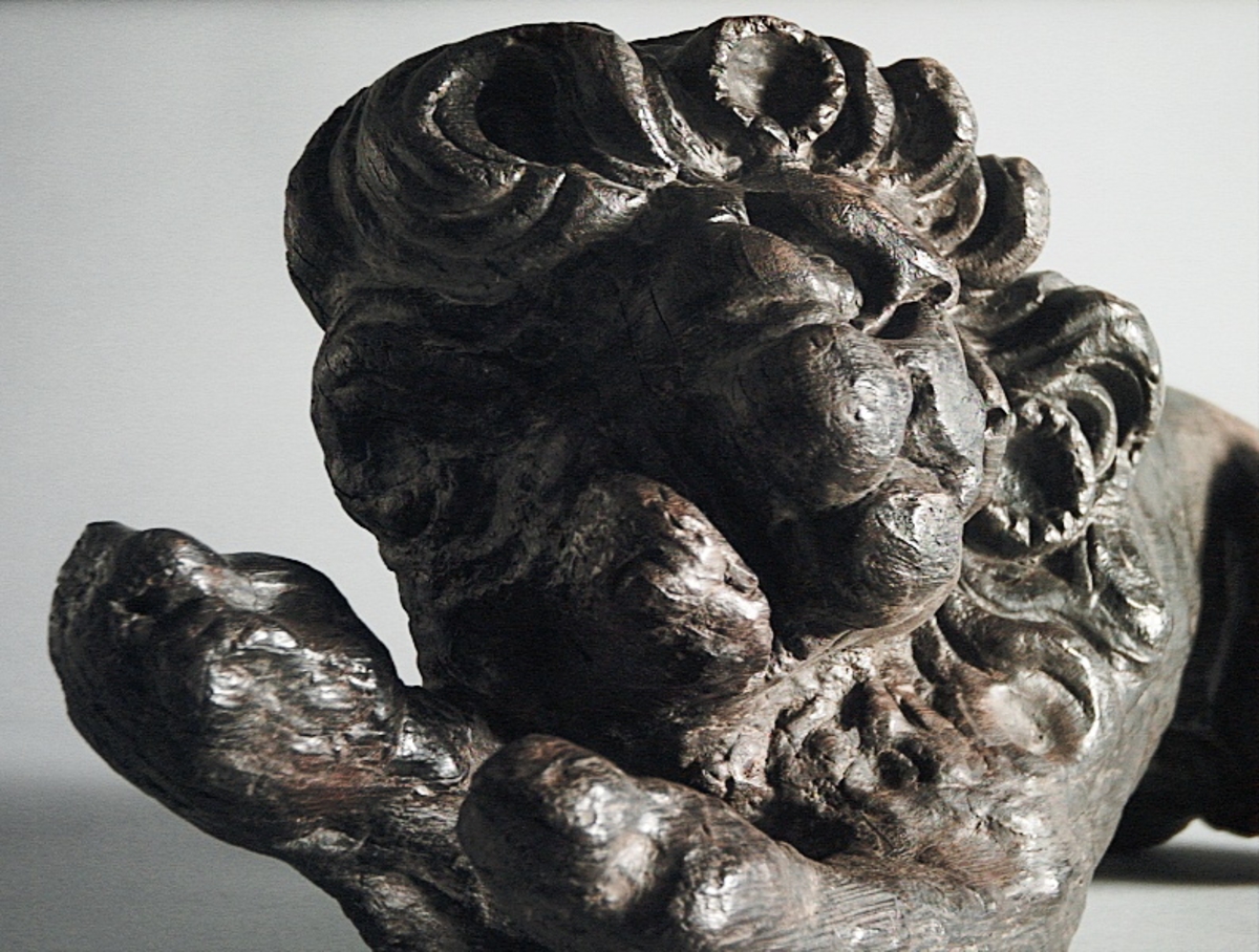 Skulptur av ett litet, liggande lejon med utsträckta framben och hopdragna bakben.
Lejonet är riktat mot vänster, sett från betraktaren. Det snett hållna huvudet återges i det närmaste i en face. Större delen av svansen saknas. Den befintliga delen av svansen avtecknar sig mot lejonets vänstra lår.

Lejonet är endast delvist rundskulpterat. På baksidan, i höjd med huvudet och höger framben, återfinns ett stort, snett urtag som bildar en slät anliggningsyta. Skulpturens framparti är således endast till hälften så tjockt som dess bakparti.
Bakkroppen är kraftigt sliten och skadad. Vänster bakben saknas, liksom större delen av svansen.

Text in English: Sculpture of a small reclining lion with its forelegs extended and its  hind legs tucked beneath its body.
Facing to the observer''s left, the head, held crookedly, is nearly en face. A large part of the tail is missing, and the remainder curves towards the left hind leg.

The lion is only partly three-dimensional. On the rear at the head height and at the right foreleg a large oblique hole forms a flat area for attachement, thus the forepart of the sculpture is thus only half as thick as its rear.
The rear of the body is badly worn and damaged. The left hind leg has been broken off.