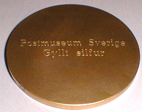 Medalj i brons med motiv av en häst med en rektangulär platta
på sadelns plats i förgyllt silver. På plattan en postsymbol ett
vänstervänt posthorn. Inskription på åtsidan: NORDIA 96, REYKJAVIK.
På frånsidan: Postmuseum, Sverige, Gyllt silfur.