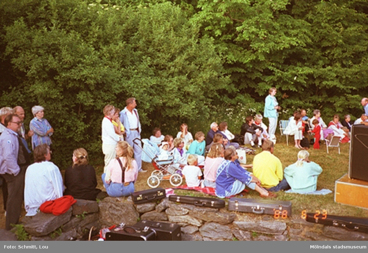 Människor som tittar på folkdans i parken vid Gunnebo slott. De sitter och står bl.a på en stenmur.