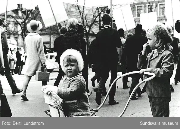 Annelie (f. 1966) och Carina Lundström (f. 1961) i korsningen Köpmangatan/Esplanaden. I bakgrunden 1:a maj-tåget på väg österut. Flickorna är döttrar till Britt-Marie och Bertil Lundström.