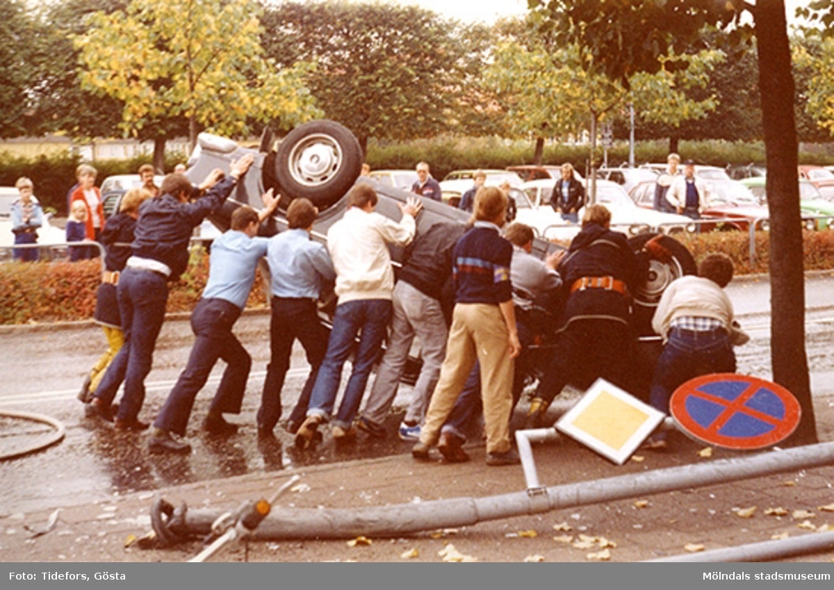 Människor hjälps åt att vända på den upp-och-ner-vända bilen, 1970-tal.