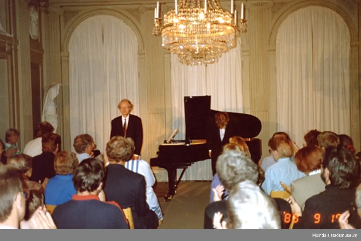 En musikkonsert inne på slottet. En man står vid ett piano, vänd mot publiken.