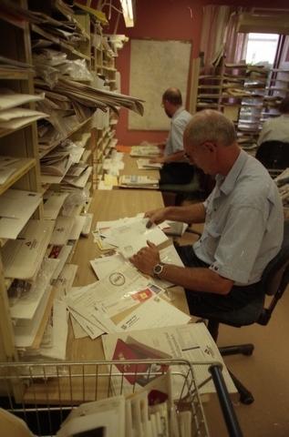 Lantbrevbärare Reinhold Andersson med flera posttjänstemän,
sorterar post inne i sorteringsdelen på en postanstalt. Tillhör en
dokumentation av en lantbrevbärare i trakten av Valdermarsvik av
fotograf Ove Kaneberg.
