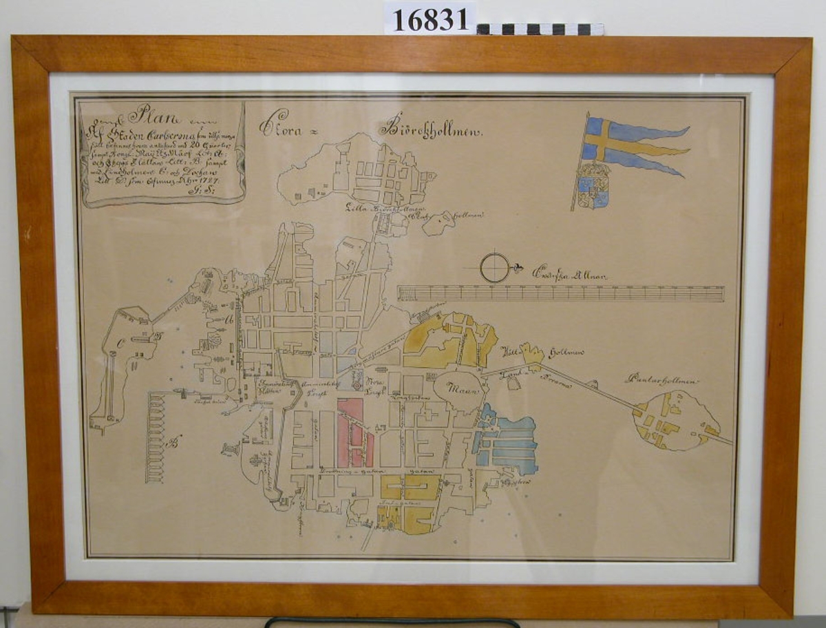 Karta inom glas och ram. Vitt papper, text  och bild i tusch och akvarell i gult, blått och rött.
Avtecknad kopia av karta från 1727, jämför K 490. Kartan visar (enligt text i höger hörn) Karlskrona stad indelat i 20 kvarter, varvet samt Pantarholmen, stora och lilla Björkholmen. Skalan i svenska alnar, där 100 alnar är 12 mm. Längst ned till höger  "av kopia C.G.H-n 1922". Ram av fernissad björk 29 mm bred. Baksida papp.