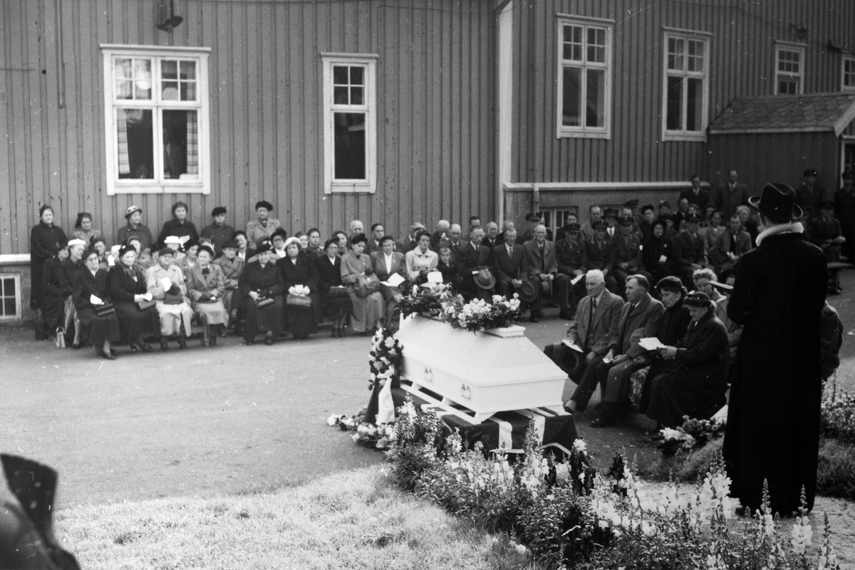 Begravelsen til Kristine Torbergsen. Kista står midt på plassen, til høyre står prost Harr.