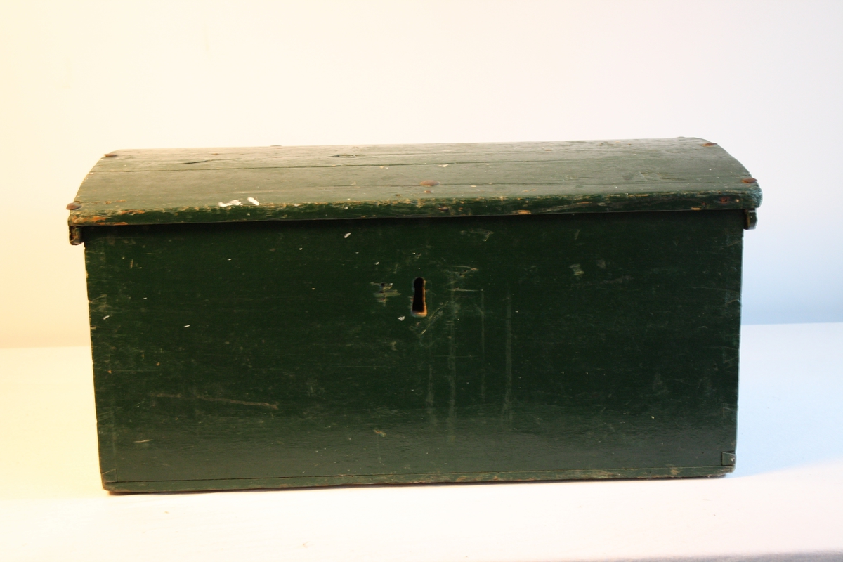 Kiste med svakt bua lok. Handtak i metall på begge sider. Metallnagler i lok.  Den er målt grøn. Sett saman med sinking. raudmålt inni. Spor etter at det har vore ein leddik.