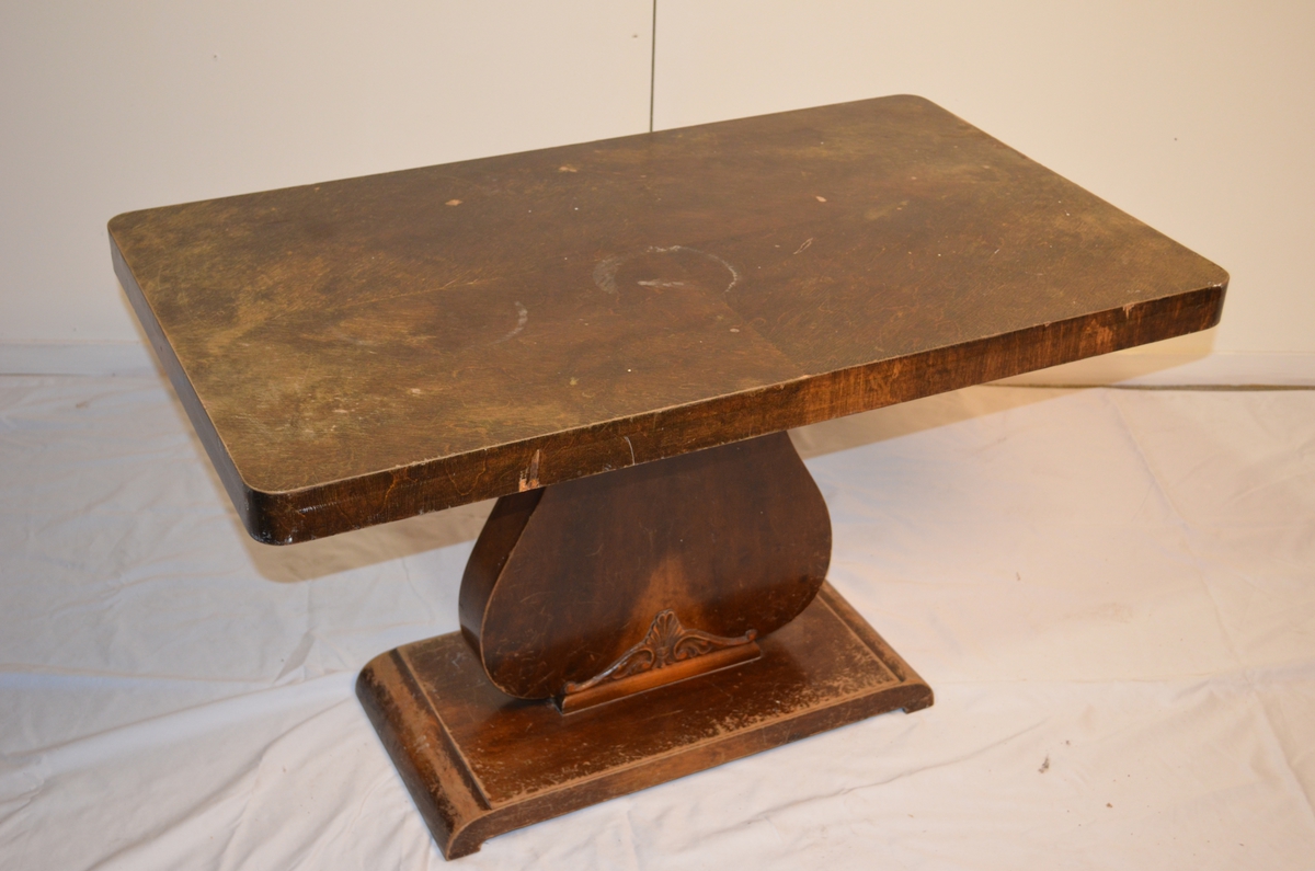 Rektangulert stuebord med ein fot. Nederst på foten er det limt fast utskjæring av tre. Flekkar og misfarging på bordplata.