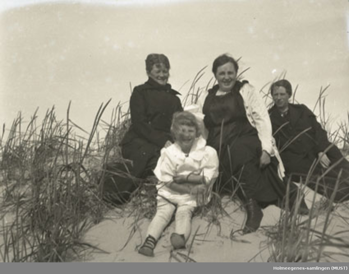 Fire personer, sitter i en sanddyne (tre voksne kvinner og en liten jente). Muligens samme sted og tidspunkt som i ST.K.HE 2007-011-0046 og -0048.