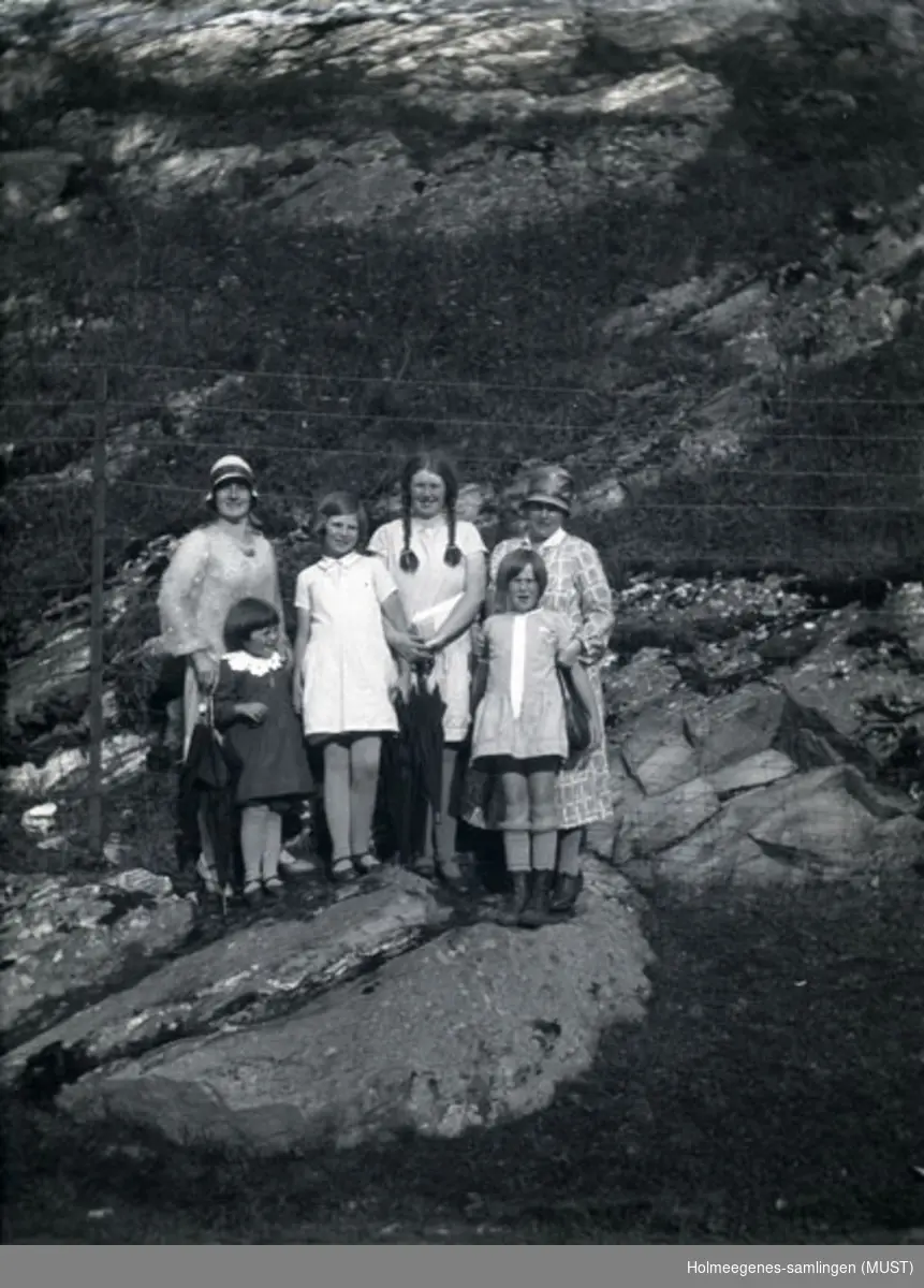 Gruppe med to kvinner og fire jenter oppstilt utendørs i sommertøy. Kvinnen helt til høyre har bøttehatt på.
