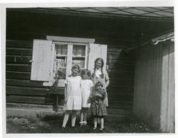 Fire jenter står ved en husvegg. Rett bak dem et vindu med s