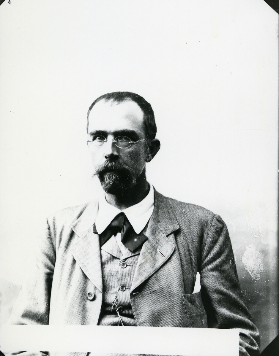 Dresskledd mann med briller, i halvfigur, lerretbakgrunn