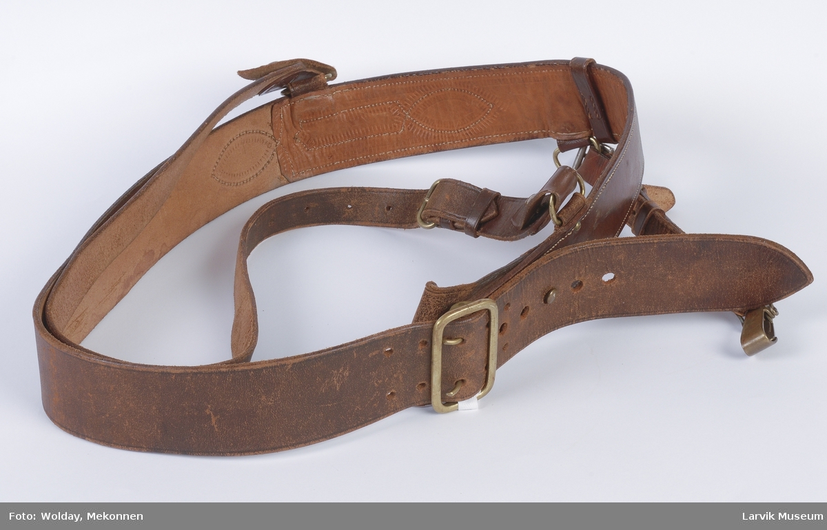 Form: Bredt belte med spenne for feste. Et smalere belte som går over skulderen.  Det brede beltet har en krok, og en stropp som henger ned.
