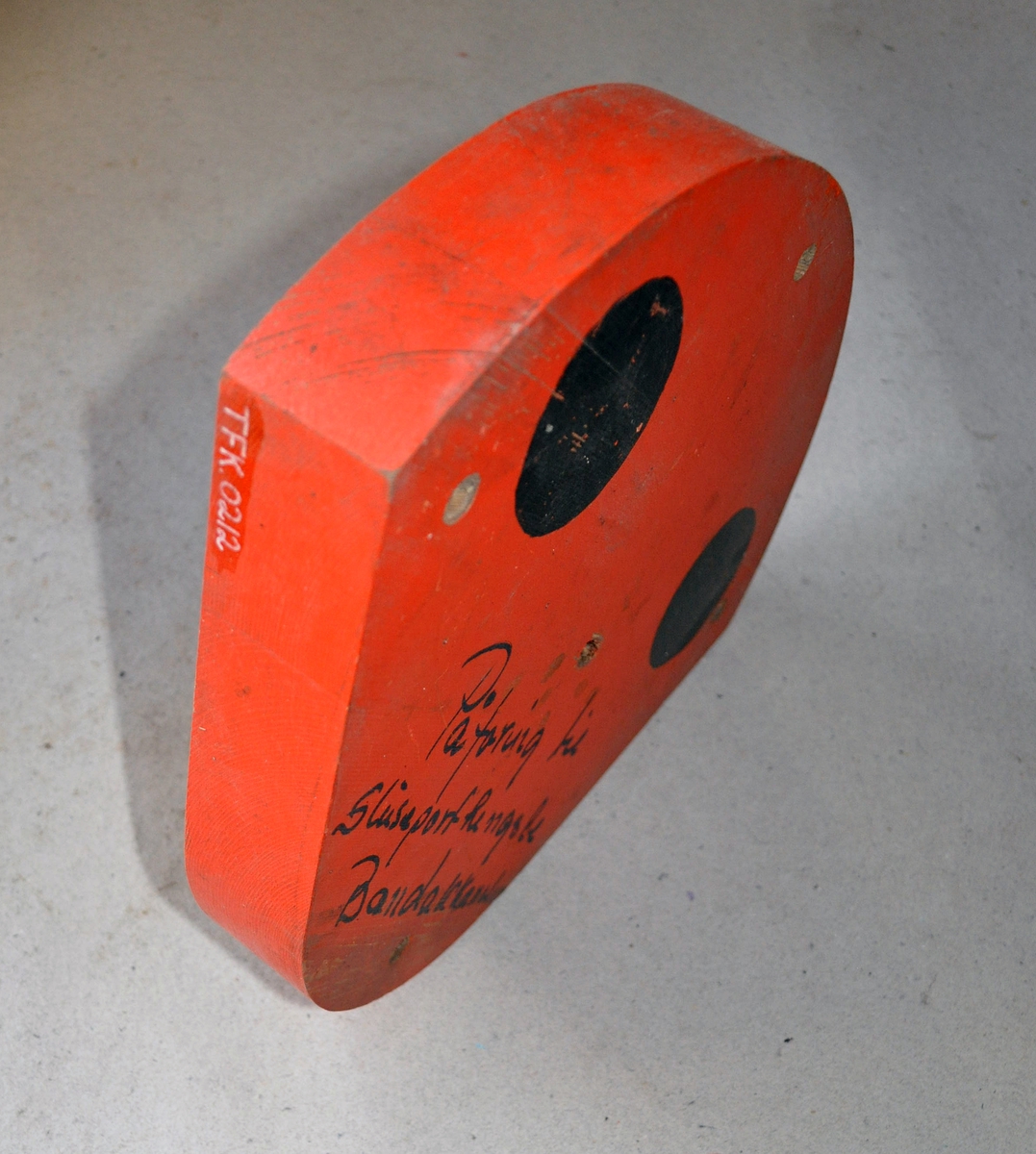 Støpemodell av tre med skruehull. Skive til å bygge opp porthengslene med. Oransj farge og to sorte prikker på.