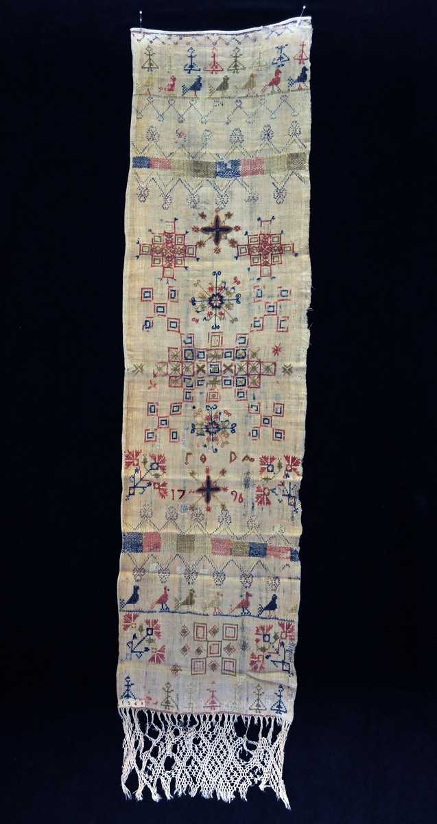 Fra protokollen: 
Haandklæde til grøtspand av hjemmelin, med fletning (defekt). Utsydd i korssting i rødt, blaat og gulgrønt. Mønsteret er symmetrisk. Fra et midtparti med adskillige bladroser og ruteroser gaar til begge sider utover følgende mønstre: tværbord av bølgelinjer i skiftende schatteringer, aapent bælte med kronesøm, række sittende fugler, række kvindefigurer, alt i skiftende farver. Sømmen meget slitt.