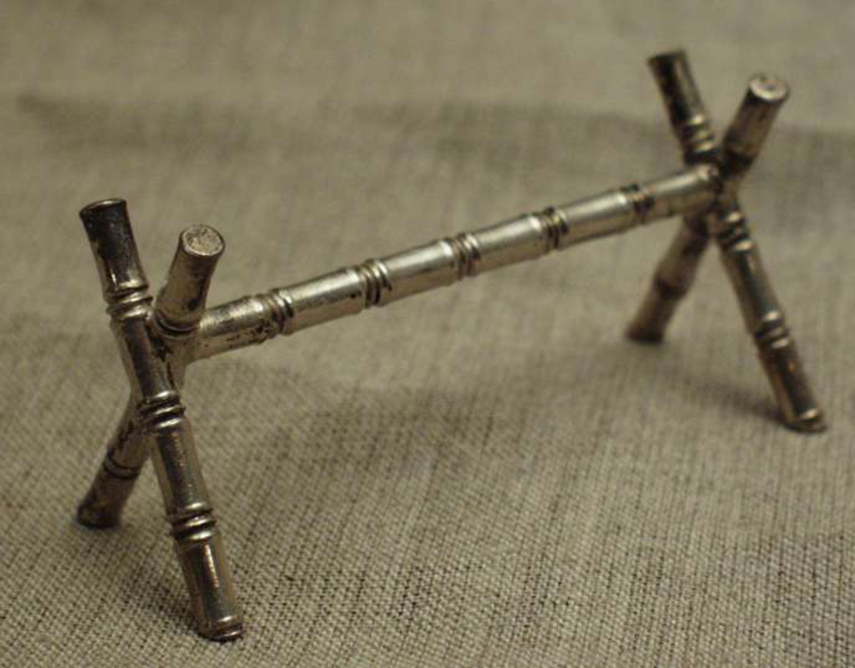 En ca 7 cm lang metallpinne holdes oppe av to metallpinner i kryss i hver ende. Alle pinnene har tre tette riller omtrent hver centimeter.