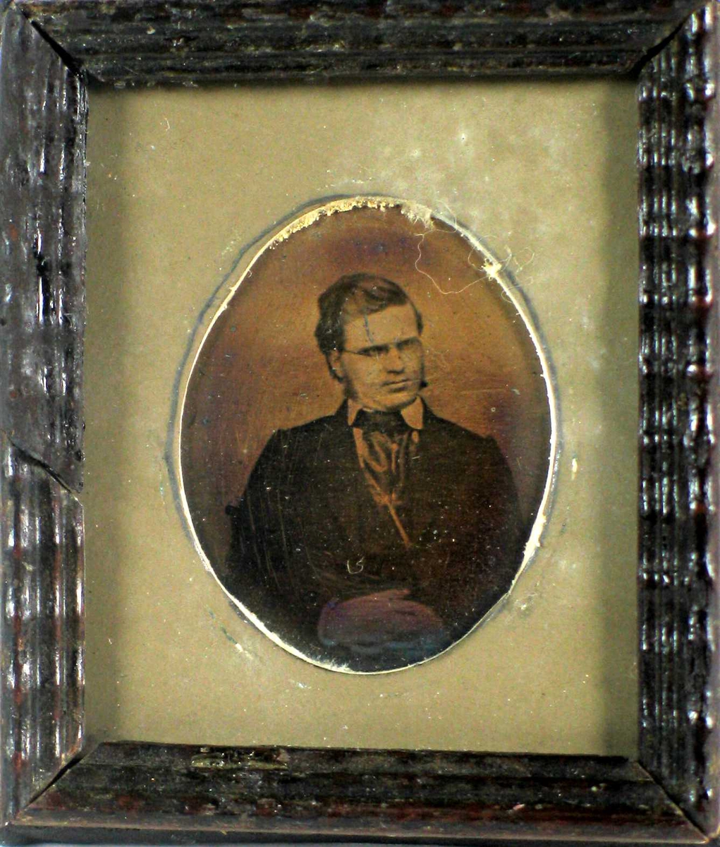 Portrett i gammel fotografiteknikk, trolig ambrotypi. Bildet har grå oval passepartout og mørk brun profilert treramme.
