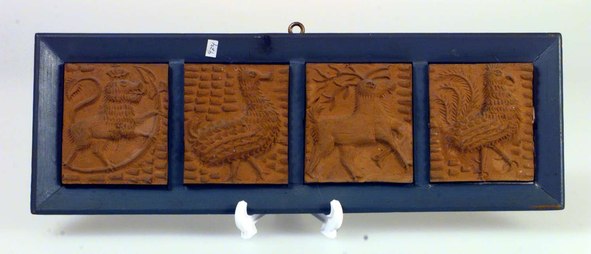 Fire avstøpninger i gips satt sammen i en treramme. Motivene er dyrefigurer - løve med krone, fugler, hjort. 