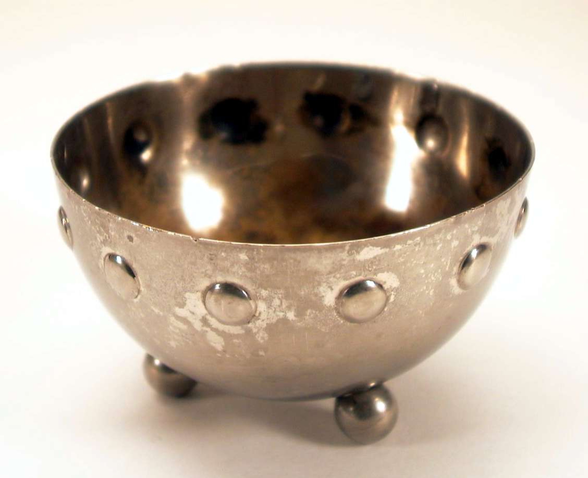 Liten, rund skål i sølvlignede metall. Skålen kan være forniklet. Skålen står på tre kuler.