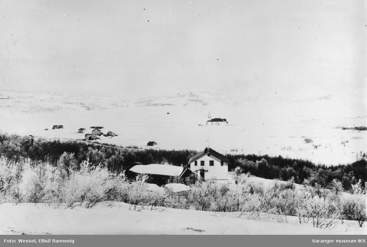 Parti av Kirkenes april 1896. I forgrunnen distriktslegeboligen Solheim og kirken i bakgrunnen. Bak til venstre i bildet ser vi kommunens tinghus, klokkergården og handelsmann Figenschous hus. Fjorden er frosset en mil utover.