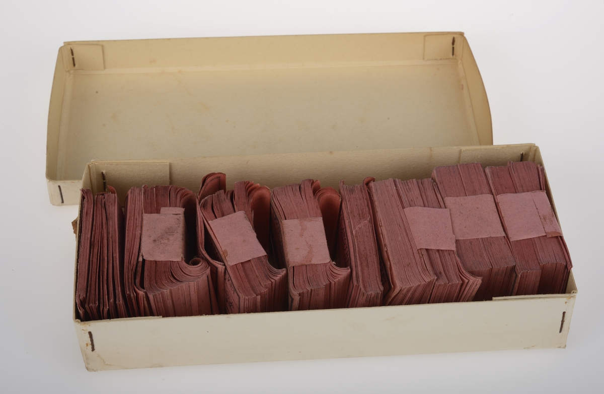 Rektangulær eske av papp med lokk inneholdene flere hundre trykte etiketter av papir.