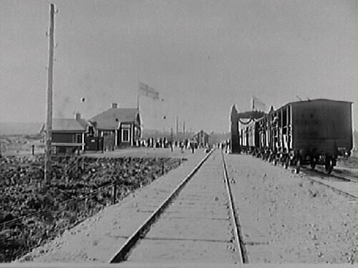 Invigning av första etappen av Varberg-Ätrans järnväg i april 1911, då banan var klar till Ullared. Två järnvägsspår och ett tåg vid Skinnarelyngen station i Svartrå socken. En grupp personer står på perrongen utanför stationsbyggnaden.