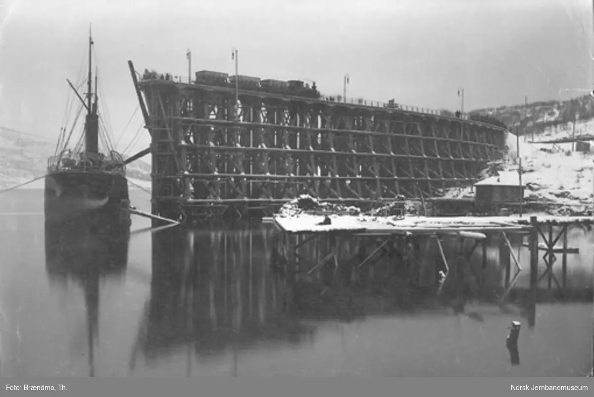 Første malmutskipning fra Narvik; damplokomotiv med malmvogner på kaien og dampskip som lastes