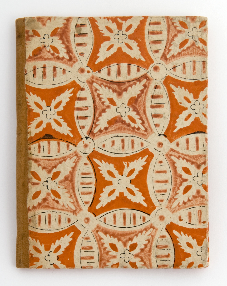 Tynn, liten bok med pappomslag, gulbrun skinnrygg og oransje-hvitt mønstrert papirtrekk