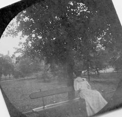 Lyskledd kvinne sitter på benk i park, ant. Oslo.