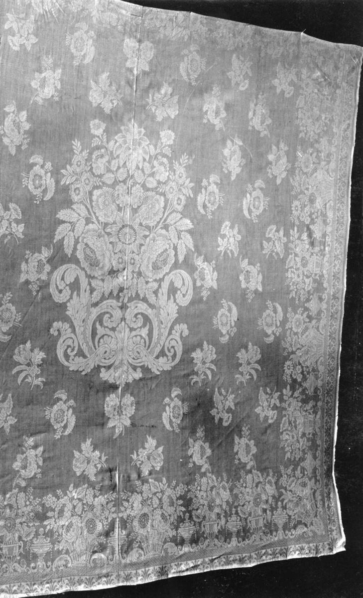 Hvit damaskduk med mønster av blomsterkurver og strøblomster. Antagelig fra Tyskland slutten av 1700-tallet.