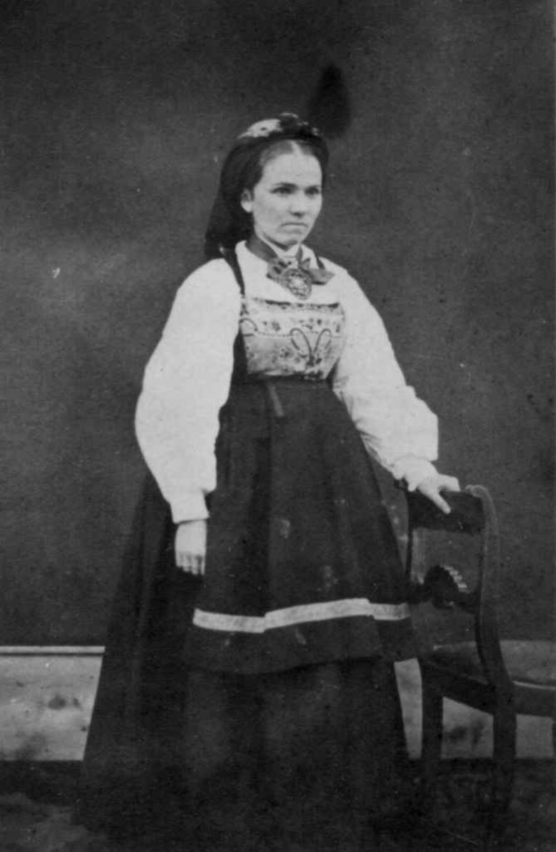 Kvinnedrakt, Vest-Telemark. 1860-årene. Azora Jensen, f. Bretville stående ved stol.
Fra serie tatt av Christian Munthe (1818-92), proprietær og landhandler, eier av gården Moen, Kviteseid. 