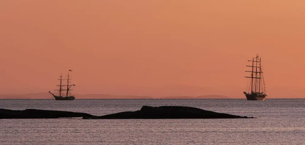 solnedgang på sjøen med to store seilbåter