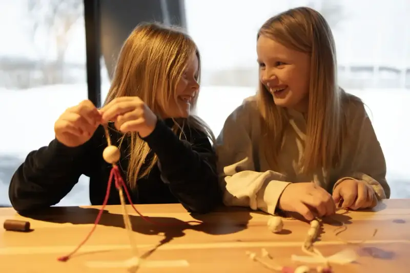 To jenter som lager makramé og smiler til hverandre