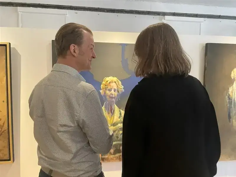 To besøkende ser på et portrett av Håkon Gullvåg i utstilling på Bogstad Gård.