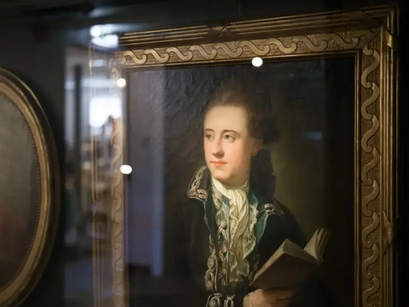 Portrait of Bernt Anker by Jens Juel, in an ornate frame. He is looking to the side, dressed in a dark jacket with embroidered collar, holding a book.