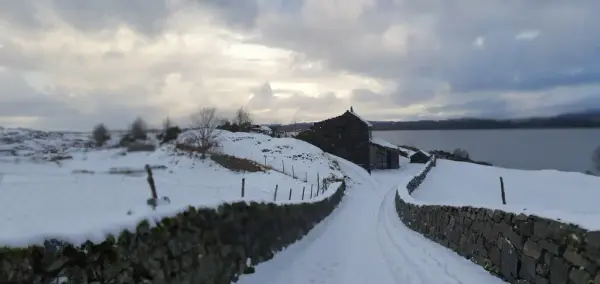 Vegen ned til informasjonsbygget, med steingard på kvar side. Det er snø.